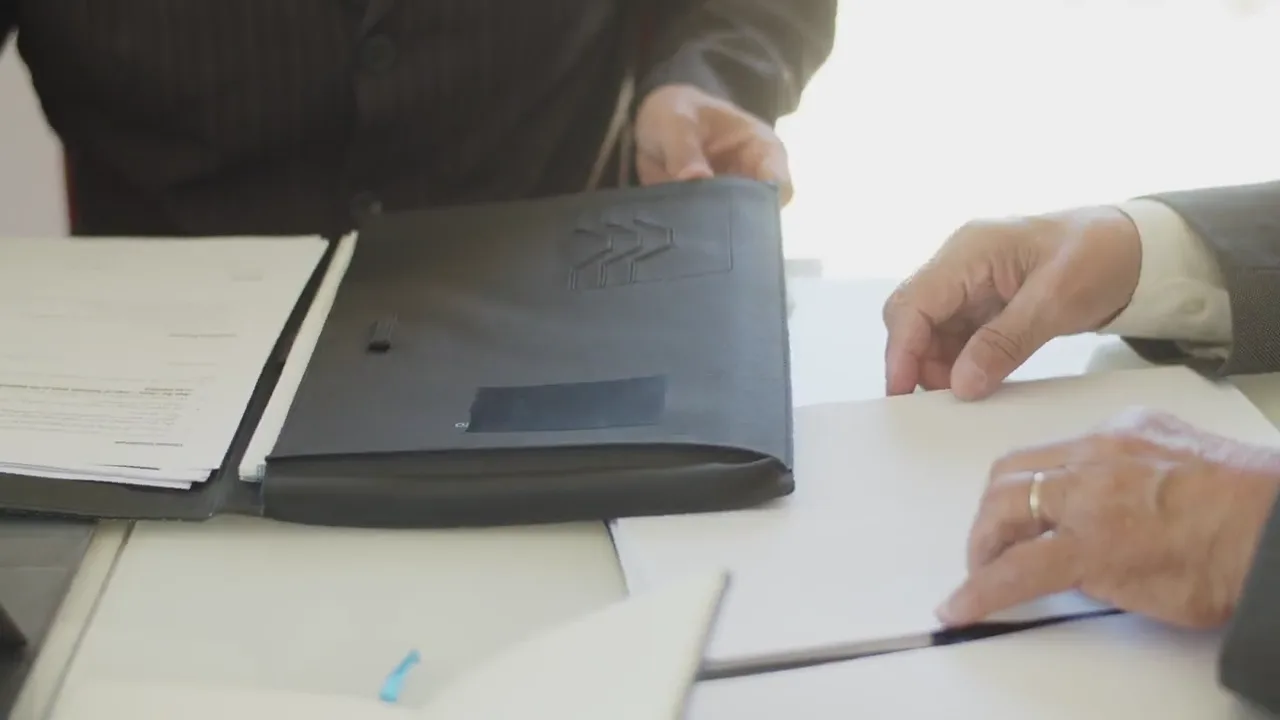 Two people exchange a document folder across a desk.